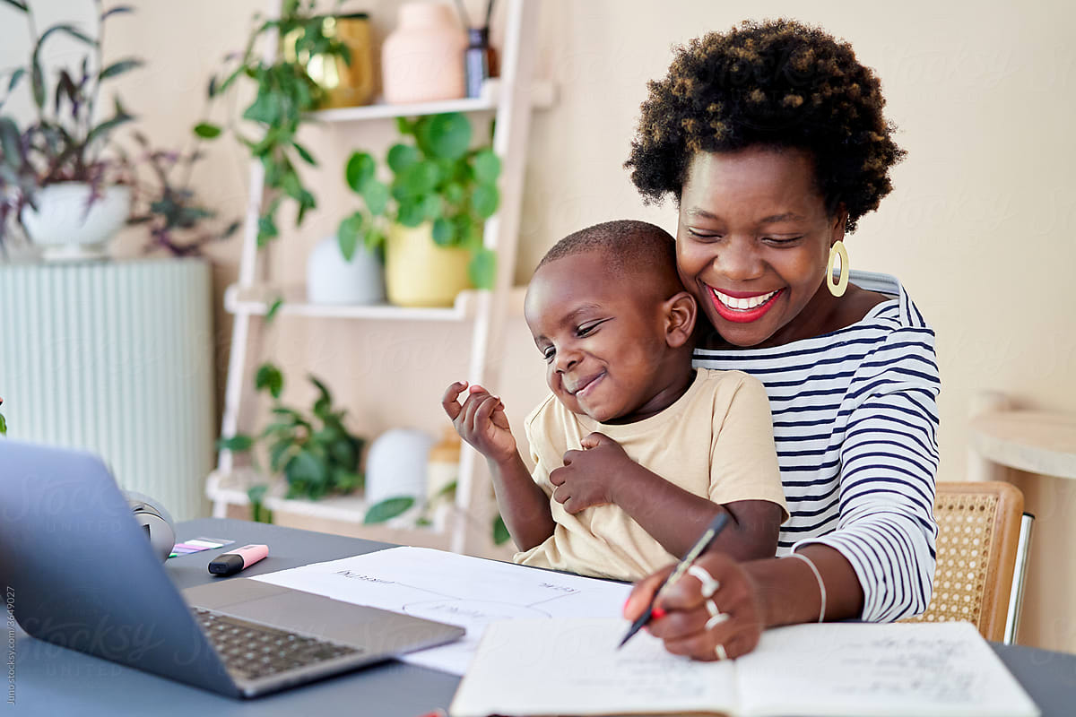 A mother working in her home office with her child sitting on her lap.