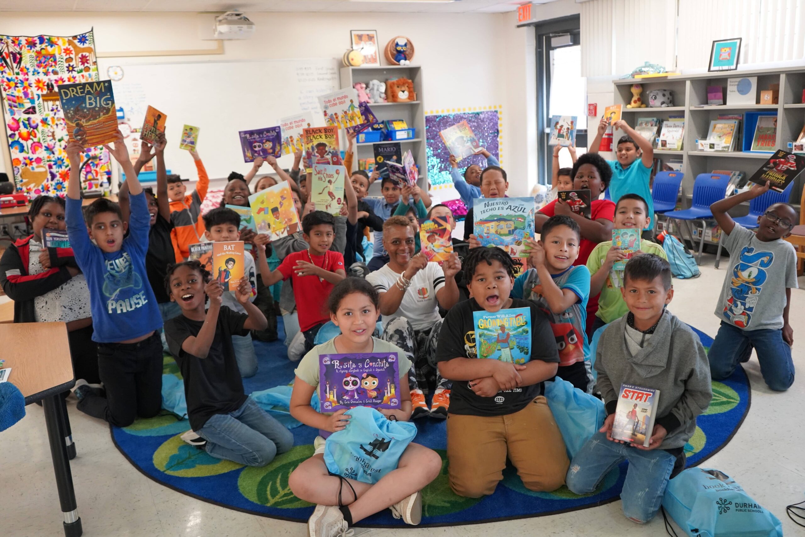 A large group of students in classroom with their teacher showing the books they selected for summer reading