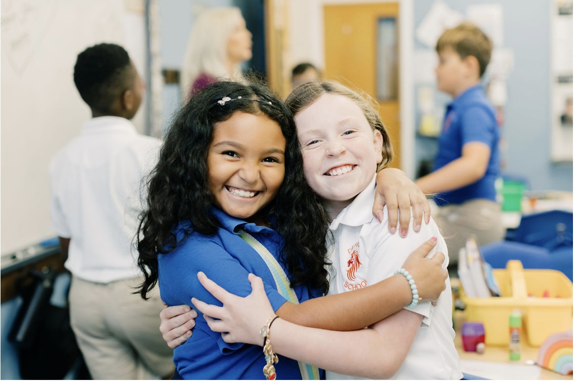 Two girls with learning differences in classroom smiling and embracing each other