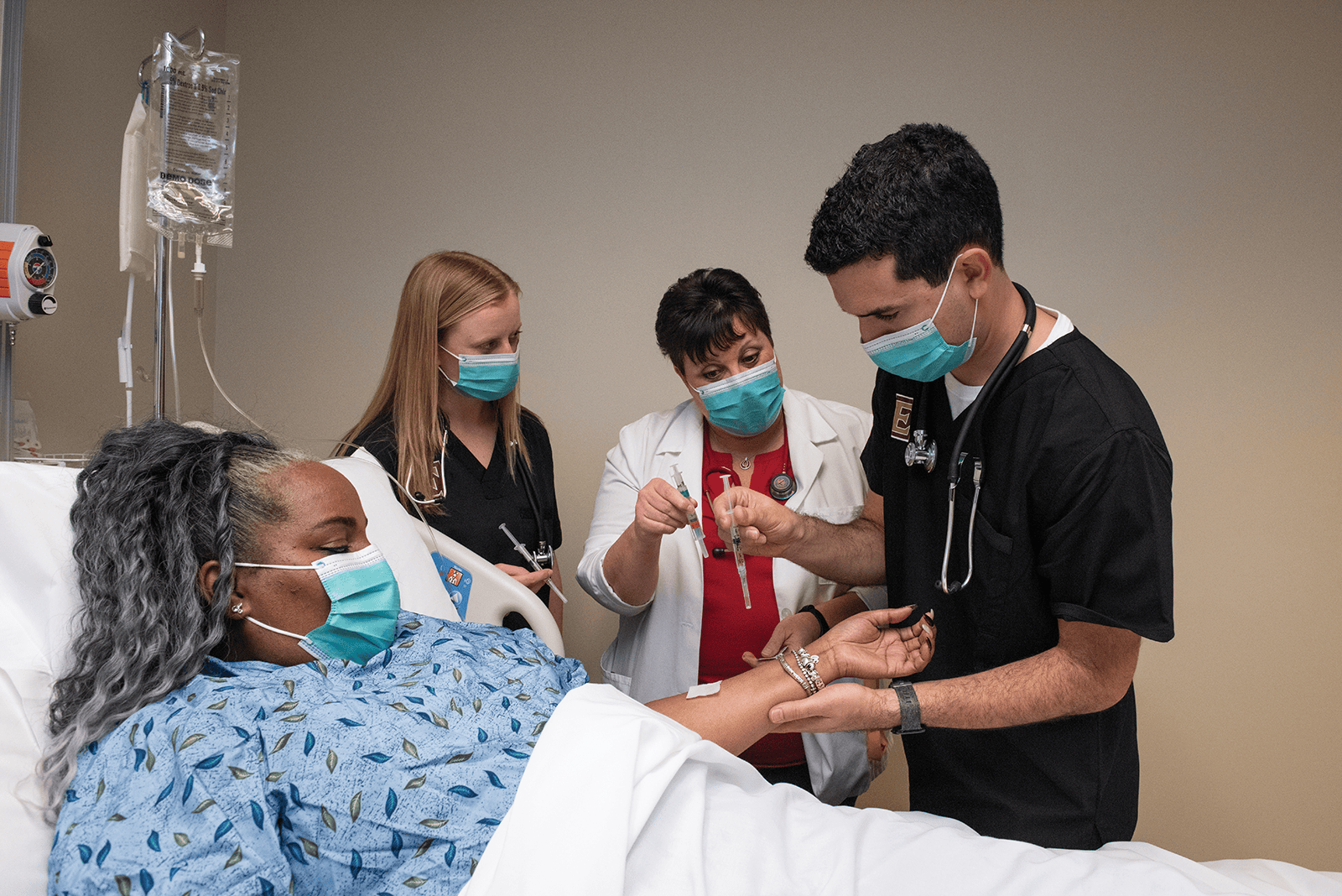 Two nursing students going through clinical training with a patient under the supervision of a professional clinician.