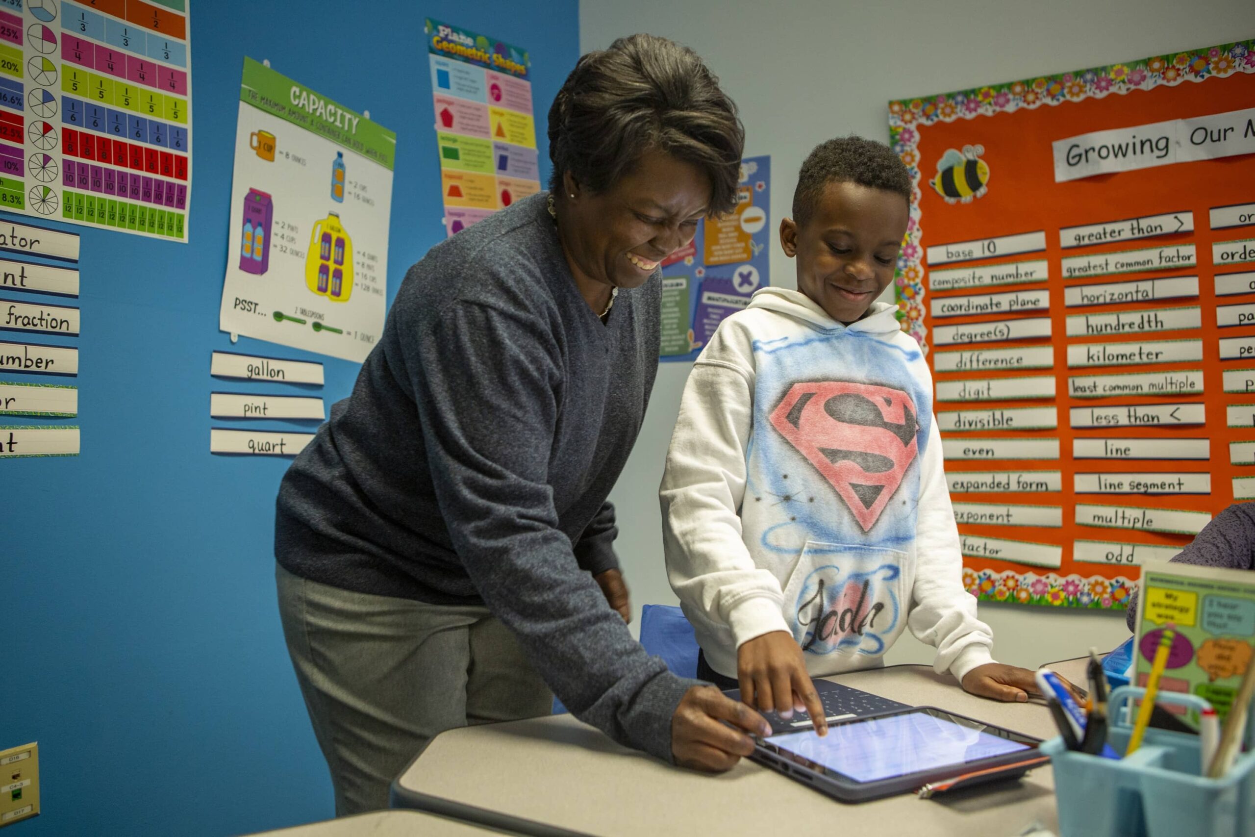 A Black teacher and a Black young boy in the classroom looking at an iPad