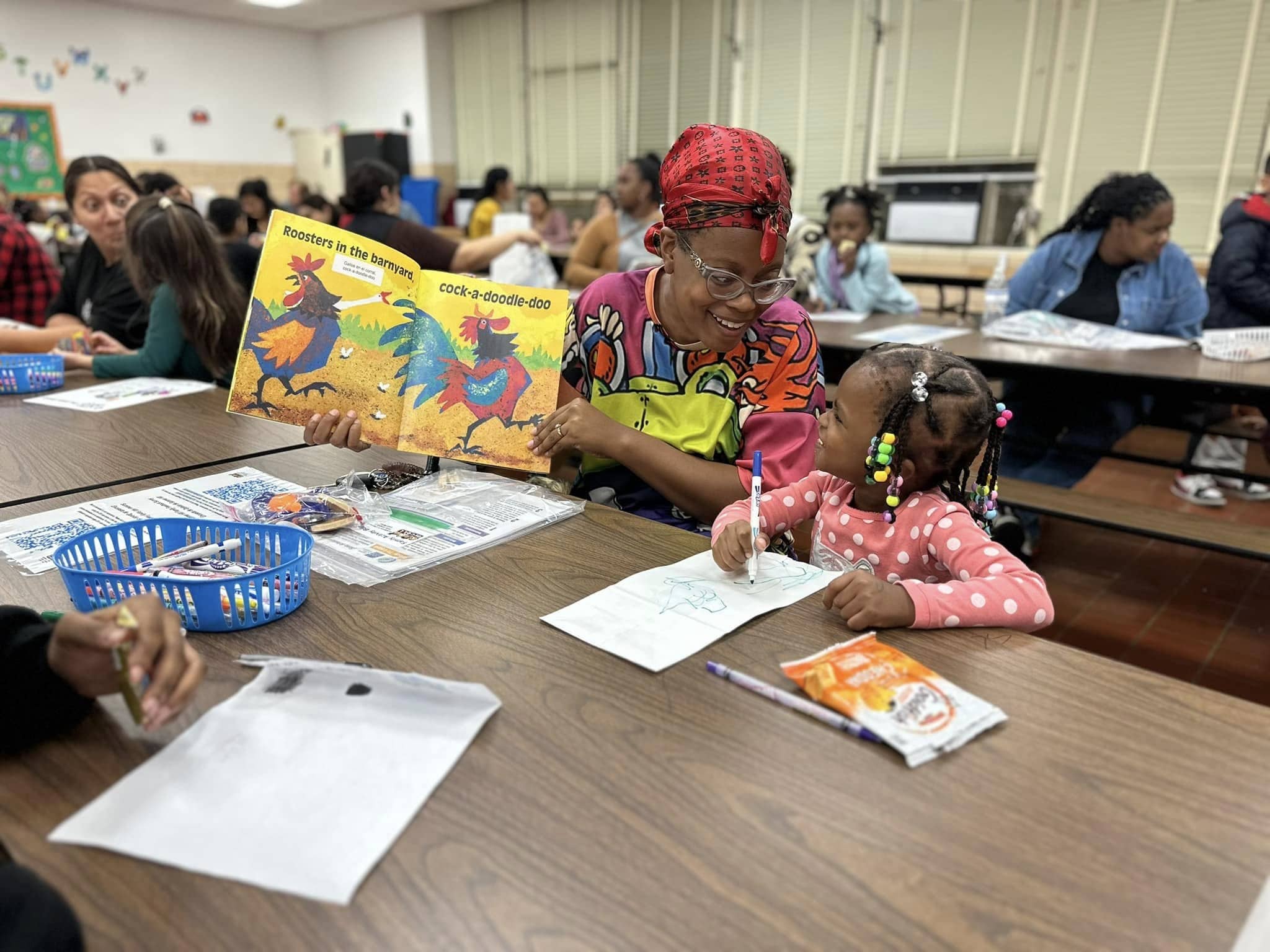 A Black mother and young daughter at a family learning center. The mother was showing colorful pages of a book to her smiling daughter.