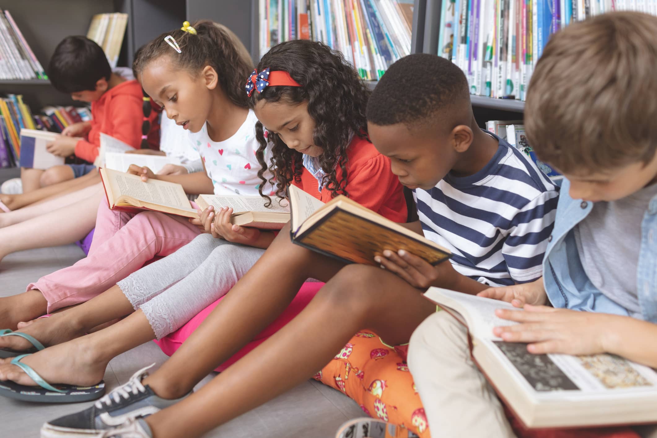 A group of diverse school kids sitting on cushions and reading books in a school library