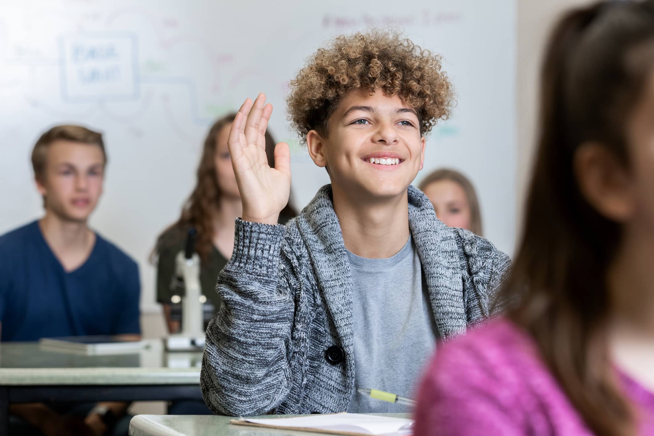 A male high school student in classroom raising his hand