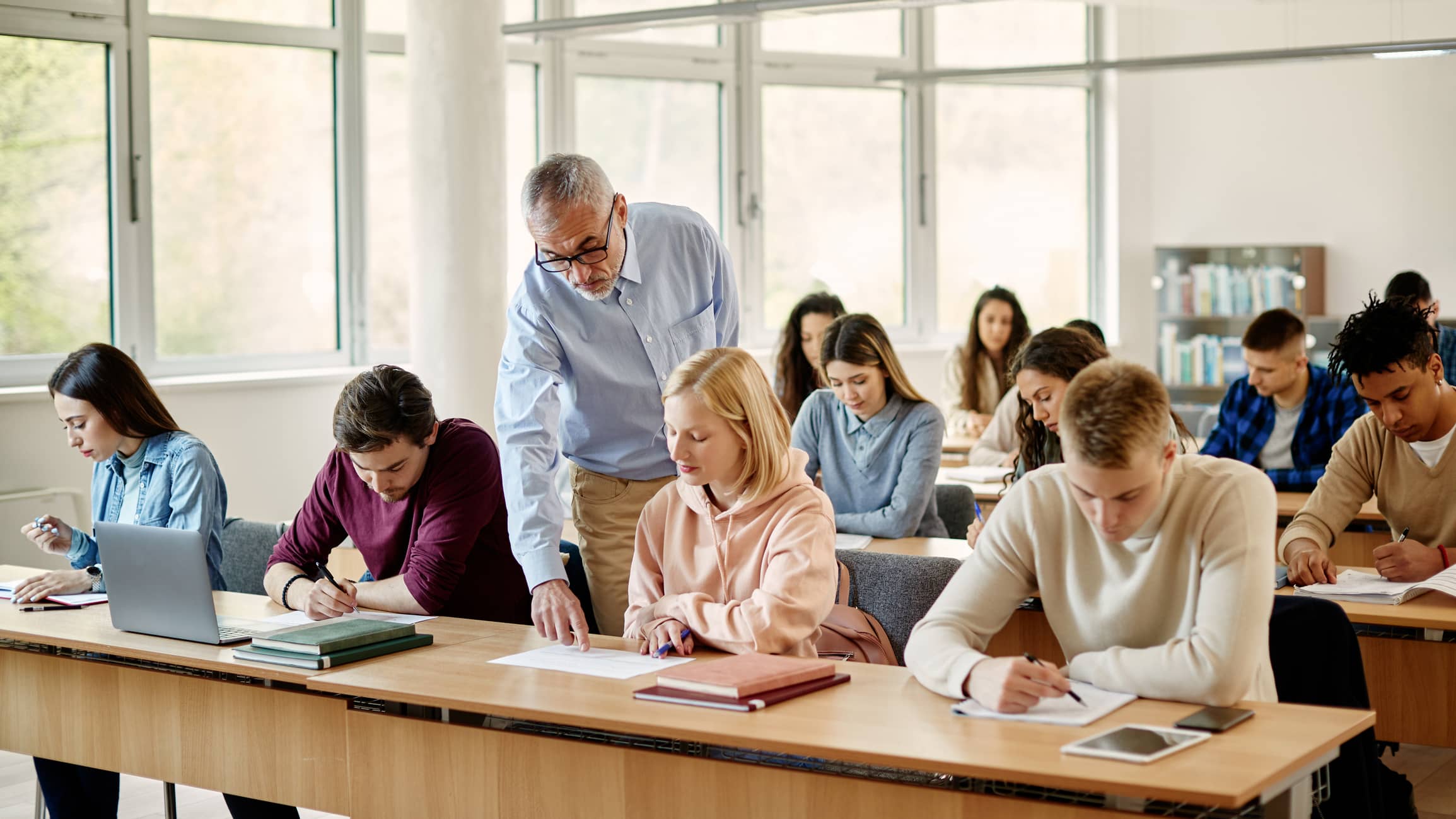 Mature professor assisting his students in class at university classroom