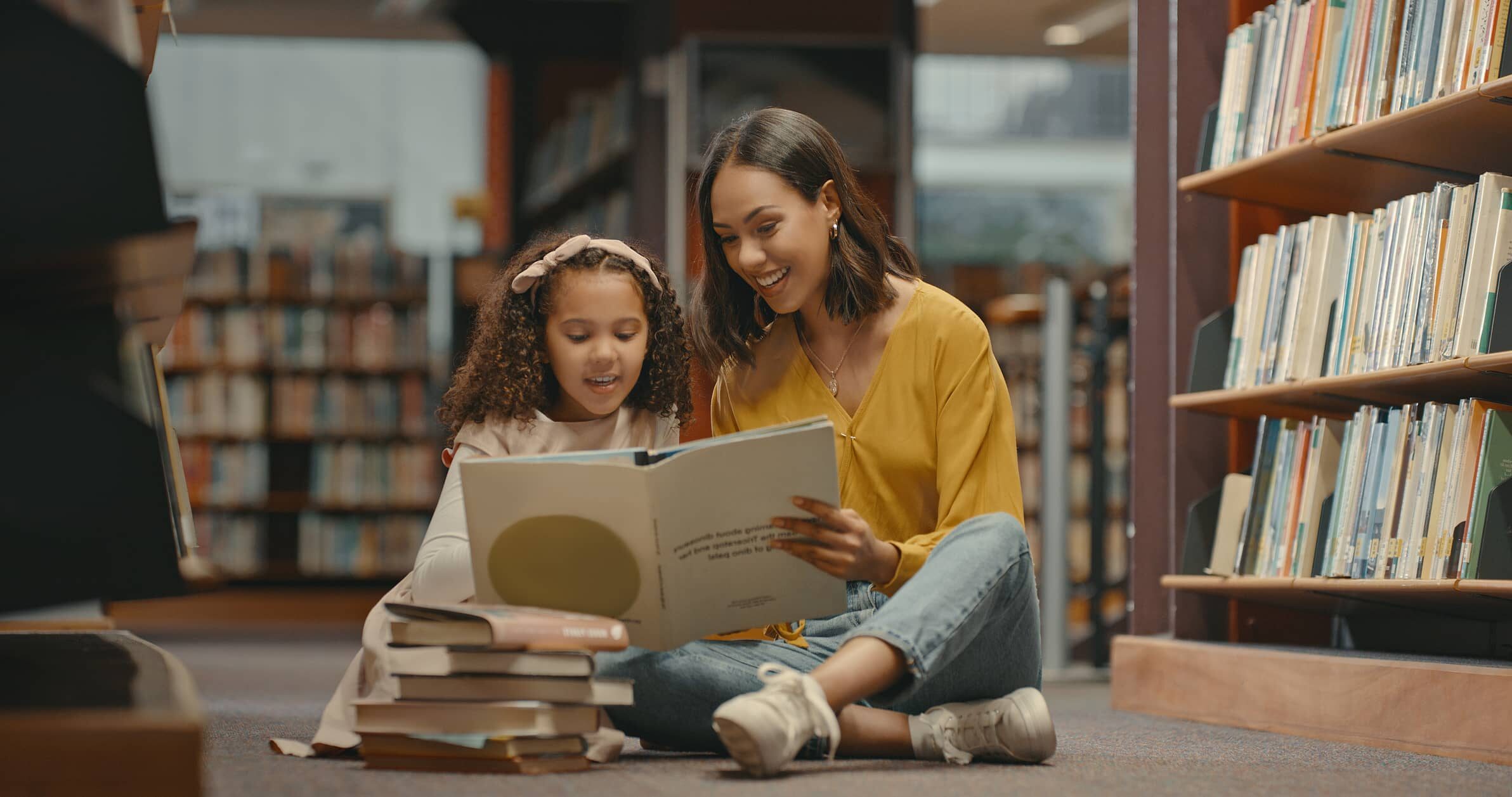 A mother and daughter sitting on the floor reading a book in the library.