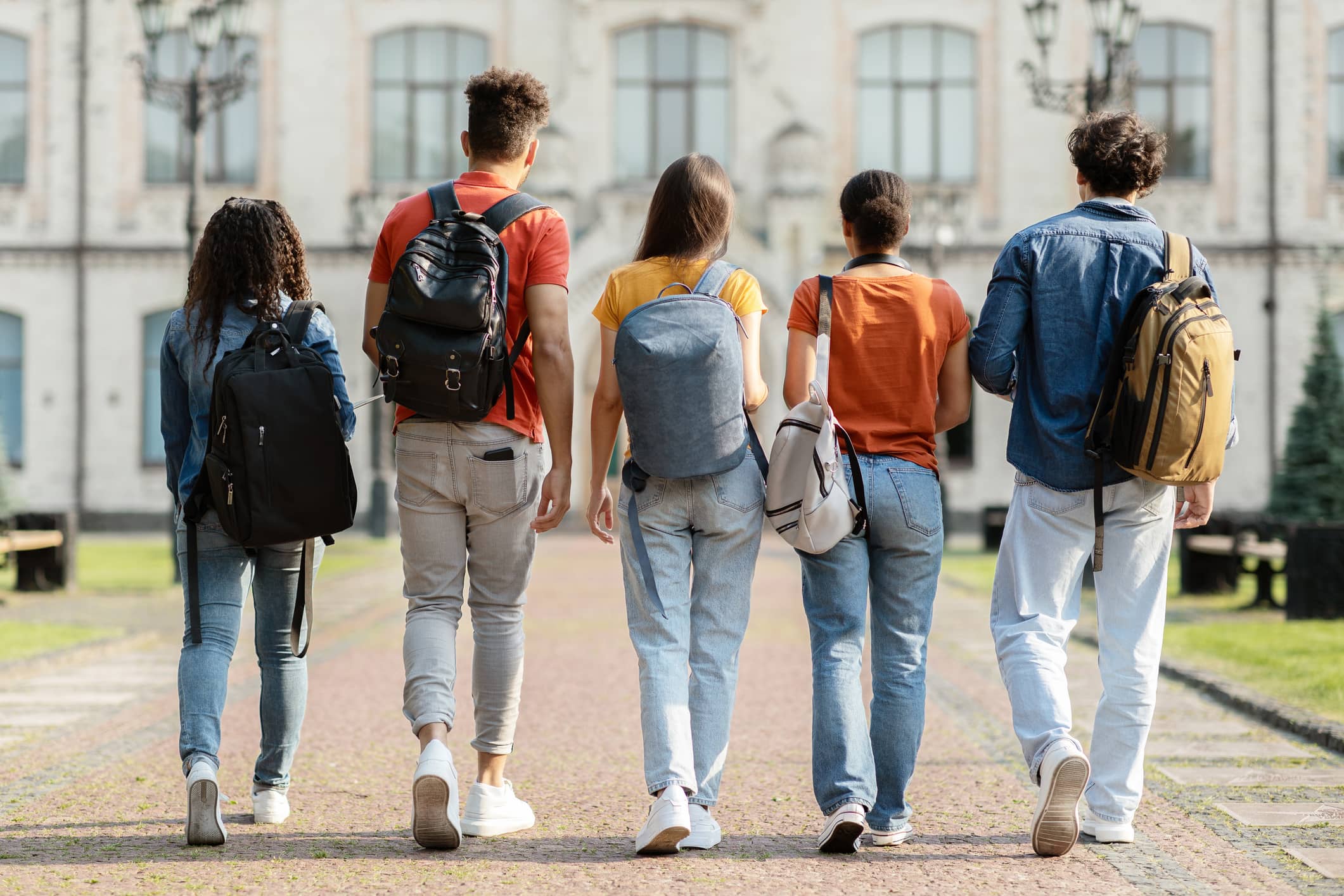 Group of five students with backpacks walking together on university campus