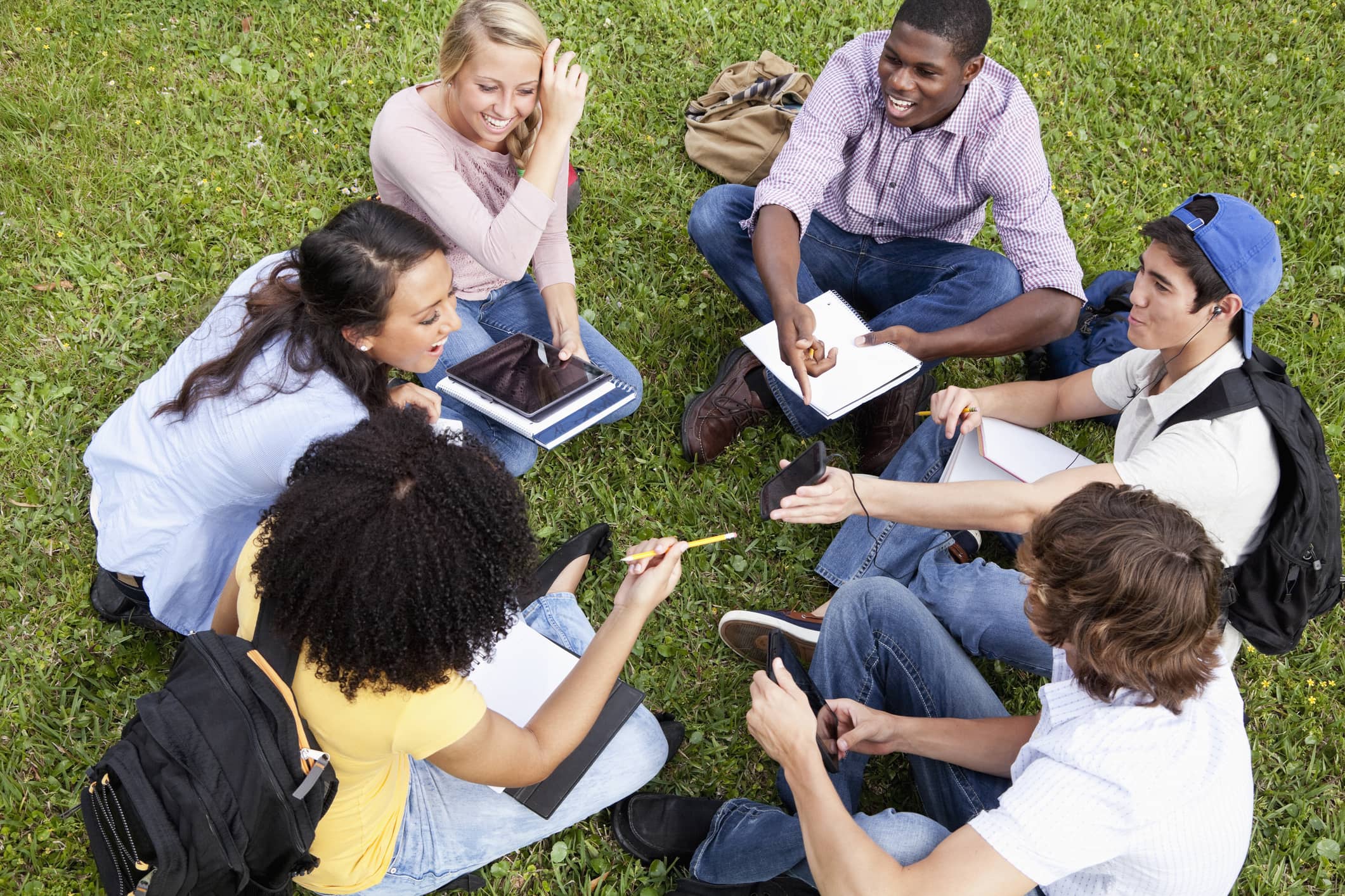 A group of six multi-ethnic college students sitting on grass studying together