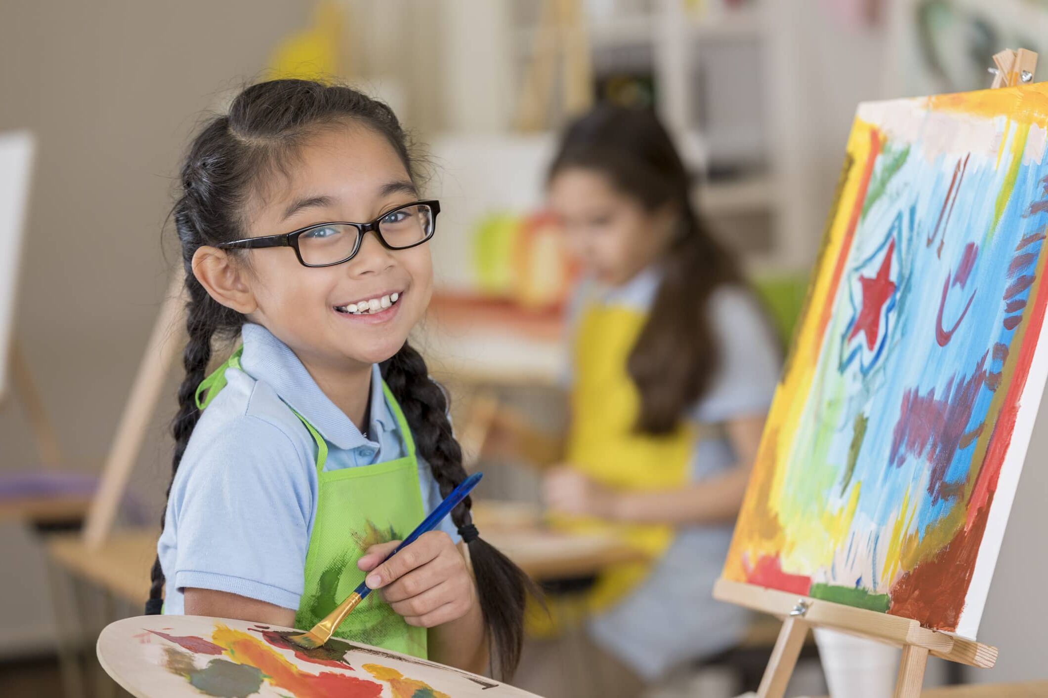 An elementary age art student smiles while working on a painting in art class