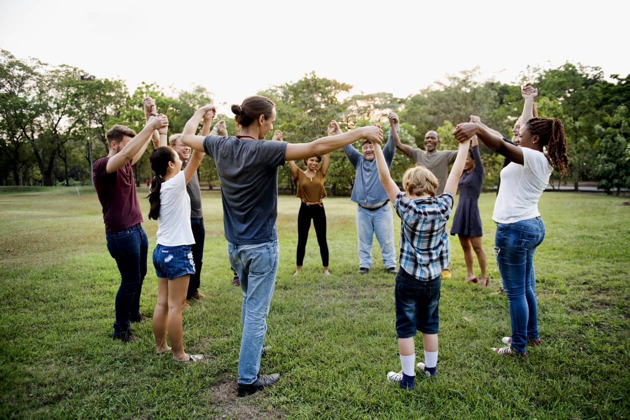 A happy group of people, adults and children, holding hands and arms up in the air at a park