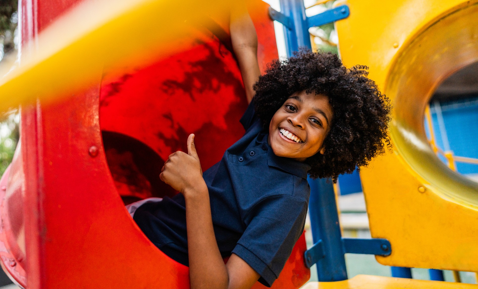 A young boy giving a thumbs up while playing at a park